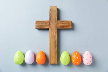 Ahşap haç ve açık gri arka planda Paskalya yumurtaları düz yatıyordu.