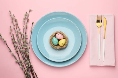 Paskalya kutlaması. Renkli yumurtalar, söğüt dalları ve pembe arka planda çatal bıçak seti olan şenlik masası.