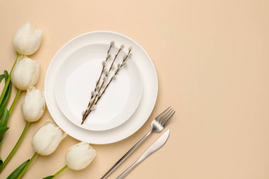 Paskalya kutlaması. Lale çiçekleri, söğüt dalları ve bej arkaplandaki çatal bıçak takımlarıyla şenlik masası, metin için yeri olan düz bir yer.