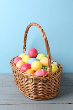 Hasır sepetin içine boyanmış Paskalya yumurtaları açık mavi arka plana karşı gri ahşap masa üzerinde
