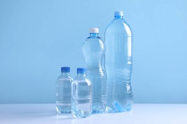 Açık mavi arka planda beyaz masada farklı boyutlarda su şişeleri