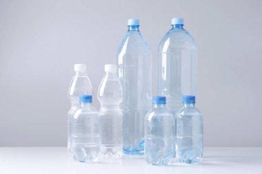 Beyaz masada gri arka planda farklı boyutlarda su şişeleri