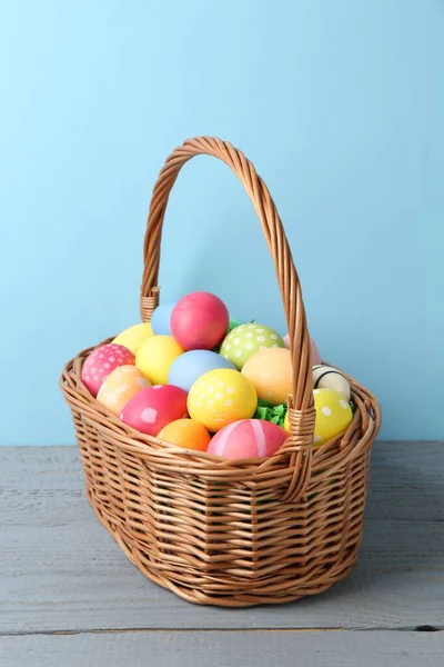 Hasır sepetin içine boyanmış Paskalya yumurtaları açık mavi arka plana karşı gri ahşap masa üzerinde