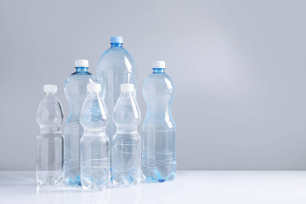 Water bottles of different sizes on white table against grey background, space for text