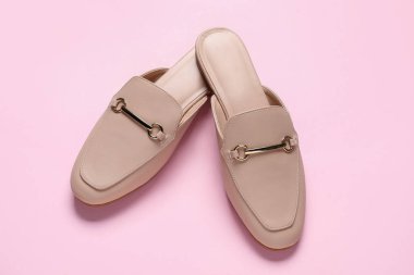 Pembe arka planda bir çift şık bej katır ayakkabısı.