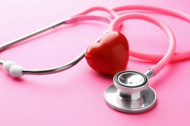 Pembe arka planda steteskop ve kırmızı kalp, yakın plan.