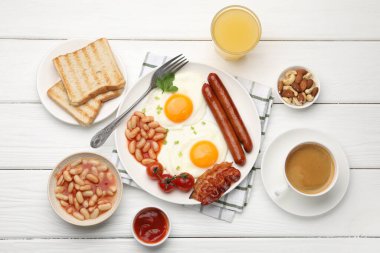 Geleneksel İngiliz kahvaltısı. Lezzetli, güneşli, domuz pastırmalı yumurta ve sosisler beyaz ahşap masada servis ediliyor.