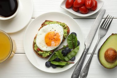 Beyaz ahşap masada servis edilen avokado tostlu sağlıklı bir kahvaltı.
