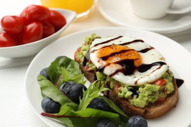Beyaz ahşap masada servis edilen avokado tostlu sağlıklı bir kahvaltı.