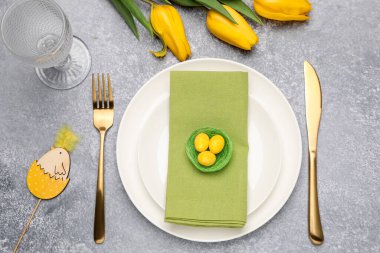 Paskalya kutlaması. Lale çiçekleri, çatal bıçak takımı ve gri desenli masa üzerine boyanmış yumurtalarla süslü bir yer.