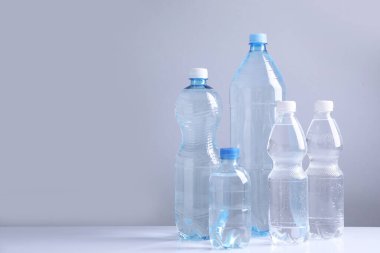 Beyaz masada gri arkaplan ile farklı boyutlarda su şişeleri, metin için boşluk