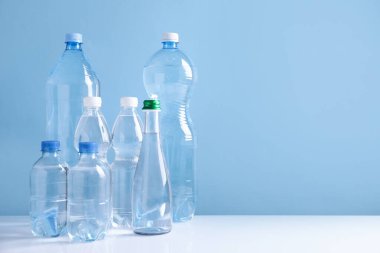 Beyaz masada açık mavi arka planda farklı boyutlarda su şişeleri var. Metin için boşluk