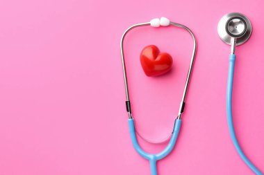 Pembe arka planda steteskop ve kırmızı kalp. Metin için boşluk