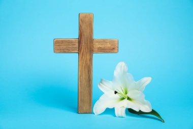 Paskalya. Ahşap haç ve açık mavi arka planda güzel zambak çiçeği, yakın plan.