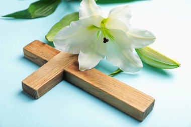 Paskalya. Ahşap haç ve açık mavi arka planda güzel zambak çiçeği, yakın plan.