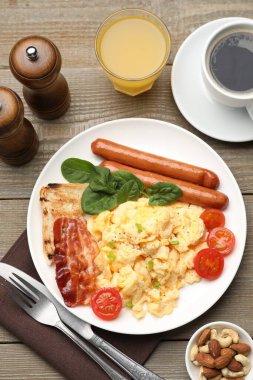 Lezzetli bir kahvaltı. Lezzetli çırpılmış yumurta, domuz pastırması, sosis ve domatesler ahşap masada servis ediliyor.