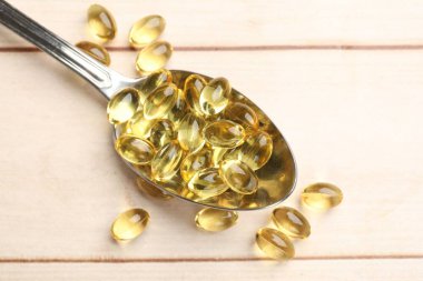 Kaşık içinde altın jelatin kapsüller beyaz ahşap masada, yakın plan