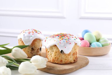 Lezzetli Paskalya pastaları, laleler ve beyaz ahşap masaya boyanmış yumurtalar, yakın plan.