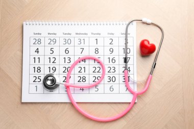 Pembe steteskop, takvim ve kalp modeli ahşap masada, düz yerde.