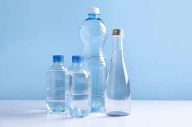 Açık mavi arka planda beyaz masada farklı boyutlarda su şişeleri