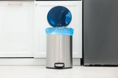 Mutfakta yerde plastik torba olan metal çöp kutusu.