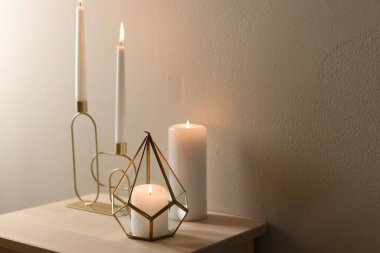 Bej duvarın yanındaki ahşap masada şamdanların içinde yanan mumlar. Metin için boşluk