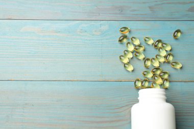 Mavi ahşap masada üzerinde altın jelatin kapsüller bulunan tıbbi şişe, düz. Metin için boşluk