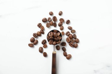 Beyaz mermer masanın üzerinde kahve çekirdekleri olan metal kepçe, düz uzanmış.