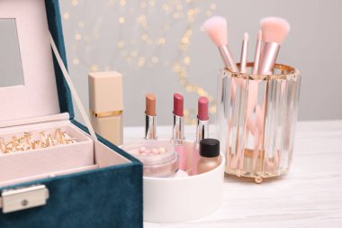 Makyaj ürünleri tutacaklarda ve mücevher kutusu açık ahşap masada gri arka planda, yakın plan. Bokeh etkisi