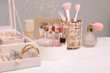 Makyaj ürünleri tutacaklarda ve mücevher kutusu açık ahşap masada gri arka planda, yakın plan. Bokeh etkisi