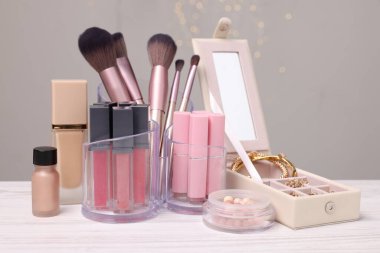 Gri arkaplana karşı hafif ahşap masa üzerindeki farklı altın mücevher kutusu ve tutacaklardaki makyaj ürünleri.