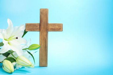 Paskalya. Ahşap haç ve açık mavi arkaplanda güzel zambak çiçekleri, metin için yere yakın çekim