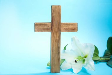 Paskalya. Ahşap haç ve açık mavi arka planda güzel zambak çiçeği, yakın plan.