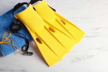 Sarı paletler, dijital kronometre, beyaz mermer masa üzerinde ıslık ve havlu, üst manzara. Yüzme aksesuarı