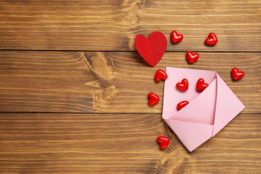 Sevgi. Ahşap masada üzerinde kırmızı dekoratif kalpler olan pembe bir zarf. Metin için boşluk