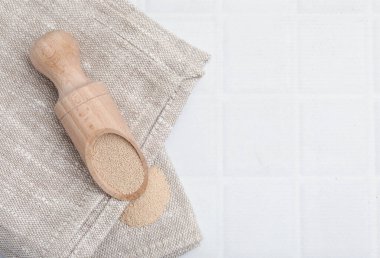 Beyaz fayanslı masada ahşap kepçe içinde kuru maya, üst manzara. Metin için boşluk