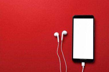 Kırmızı arka planda kulaklığı olan akıllı bir telefon. Metin için boşluk
