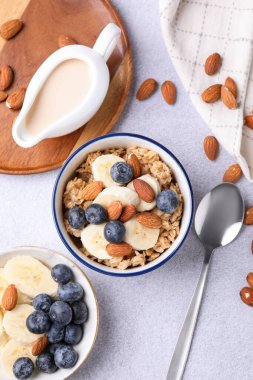 Yulaf gevreği, badem sütü, fındık, muz ve yaban mersini açık gri masada, düz yatıyordu.