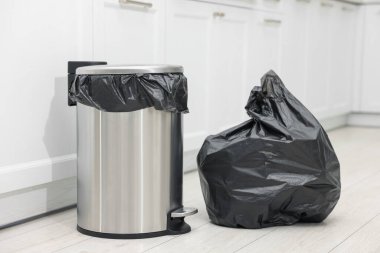 Mutfakta yerde çöp olan metal çöp kutusu ve plastik torba.