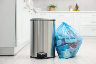 Mutfakta yerde çöp olan metal çöp kutusu ve plastik torba.