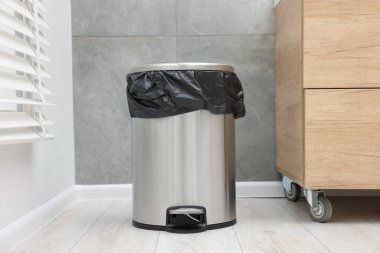 Kapalı mekanda yerde plastik torba olan metal çöp kutusu.