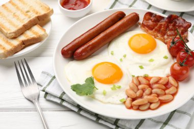 Geleneksel İngiliz kahvaltısı. Lezzetli, güneşli, pastırmalı yumurta ve sosisler beyaz ahşap masada servis ediliyor, yakın plan.