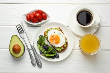 Beyaz ahşap masada servis edilen avokado tostlu sağlıklı bir kahvaltı.
