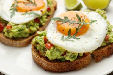 Lezzetli avokado tostları, yumurta ve roka tabakta, yakın plan.