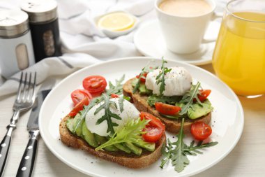 Avokado tostlarıyla lezzetli bir kahvaltı ve hafif ahşap masada servis edilen haşlanmış yumurtalar, yakın plan.