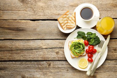 Tahta masada servis edilen avokado tostlu lezzetli bir kahvaltı. Metin için boşluk