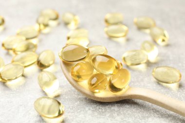 Açık gri masada altın jelatin kapsüllü kaşık, yakın plan.