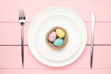 Paskalya kutlaması. Çatal bıçak takımı ve pembe ahşap masaya boyanmış yumurtalarla şenlikli bir ortam.