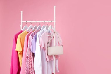 Farklı kıyafetler ve çantalar pembe arka planda asılı, yakın plan. Metin için boşluk