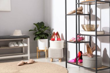 Ayakkabı bankı, farklı ayakkabılar, raf ünitesi, aksesuarlar ve açık gri duvarın yanındaki ev bitkisi.